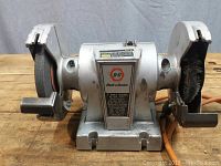 Front view of Black & Decker bench grinder showing hard grinding wheel and wire wheel, tool rests, and base.