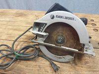 Front angle view of the saw showing blade covered by metal guard with visible rust on blade. Thick power cord coiled beside tool.