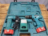 Full set including cordless flashlight, cordless drill, charger, and molded carrying case laid open on wooden surface