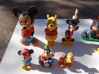 View of 10 assorted plastic Disney characters including figurines and piggy banks laid on a white background outdoors.