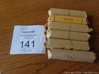 Six sealed rolls of 1965 pennies stacked together in brown paper wrappers showing the year stamped on the ends.