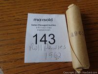 Photo of a full roll of 1962 Canadian pennies wrapped in original brown paper with the year 1962 printed on it, alongside a maxsold auction bid card.