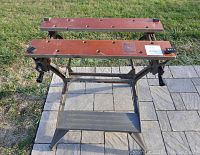 Front view of the portable workbench showing wooden clamping top and metal frame with footrest.