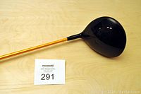 Full view of the PING i15 golf driver showing the orange shaft and black clubhead.