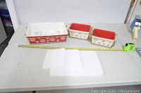 All 9 pieces laid out: three ceramic dishes (one large rectangular, two smaller squares), three white ceramic lids, and three gold-tone wire racks, with measuring tape.