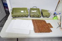 View of all components including 4 ceramic dishes with wire racks, 4 white ceramic lids stacked, and 4 woven rattan trivets on a table.