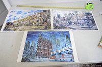 Three numbered prints by Graham Walton laid on table showing Toronto city scenes, including The Old Galway Arms pub, Flatiron Building, and streetcars.