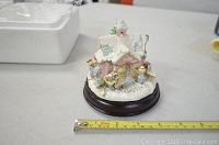 Snowy pink house figurine with three children figures and Christmas decorations on a wooden base, approximately 5 inches wide.