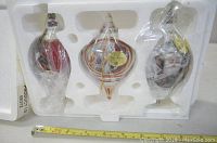 Three porcelain Christmas ornaments in styrofoam packaging, each wrapped in plastic for protection. Includes bird, teardrop shape with painted scene, and Santa Claus figure.