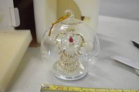 Crystal angel inside clear glass globe ornament with gold and red details, showing size with measuring tape.