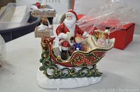 Front and side view of the porcelain figurine showing Santa Claus in sleigh with children, Christmas gifts, and a post sign.