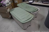 Photo of two large storage totes with lids placed side by side on a concrete floor surrounded by storage boxes and other items.