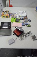 Photo of lot showing the assorted Nintendo consoles and game cartridges spread out on table including 2DS XL, DS Lite, Game Boy Pocket, and various Nintendo game cartridges and packaging.