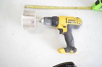 Side view of yellow and black DeWalt cordless drill with attached large metal hole cutter bit and a measuring tape alongside for size scale.