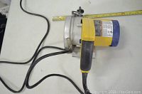 Handheld yellow and black tile saw with visible power cord and ergonomic handle, lying on a flat surface.