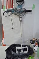 Full view of Makita electric drill with attached mixer paddle and cord wound around handle, displaying signs of use with dried residue on paddle.
