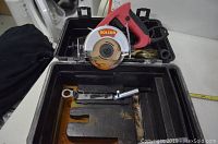 View of Bolton tile saw resting in an open carrying case displaying the tool, blade, and included accessories like a wrench and mounting hardware.