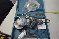 Full open carrying case containing Makita angle grinder, cutting disc in packaging, wrench, screwdriver, and some small accessories