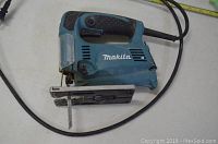 Side view of a blue Makita jigsaw showing handle, blade, power cord, and base plate.