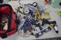 Wide view of assorted tools including screwdrivers, hammer, drill, measuring tape, and others spread out next to a red Apollo tool bag.