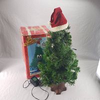Artificial Douglas Fir singing Christmas tree approximately 2 feet tall with Santa Claus style hat on top. Also shows original box in poor condition and black power adapter.