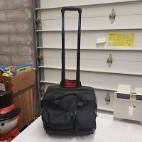 Front view of black rolling laptop briefcase on wheels with telescoping handle extended, showing zippered compartments.
