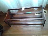 Front view of the wooden shoe rack placed on a wooden floor near a window with sheer white curtains.