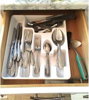 Drawer with silver-tone metal cutlery including dinner knives, forks, spoons, and teaspoons, plus a metal citrus press and a metal grater.
