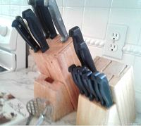 Two wooden knife blocks on marble countertop. One block contains mostly larger knives, the other contains six steak knives and several smaller knives. Black handles on all knives.