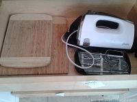 Oster hand mixer with attached electric cord and two wooden cutting boards side by side on a flat surface.