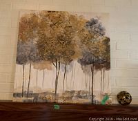Tree scene print on stretched canvas showing trees with textured leaves in grey and ochre hues, mounted on a brick wall with a decorative glass orb beside it.