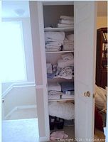 Shelf with multiple folded blankets, towels, sheets, and comforter in white/light colors