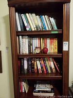 Books on upper three shelves of wooden bookcase, showing a wide variety of titles and hardcover and paperback bindings.