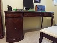 Frontal view of desk showing dark wood finish, curved ends, central keyboard drawer, and closed left cabinet door
