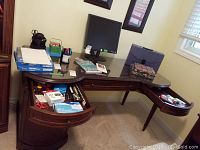 Overview of wooden desk with office items and accessories visible on drawers, desk surface, and under monitor stand