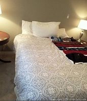 Queen bed made up with the double-sided comforter showing grey and white floral pattern on top and 3 pillows arranged at head of bed, two in pillowcases and one sham; bedside tables and lamps visible