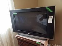 Front view of LG 30 inch CRT TV on wooden stand with remote on top