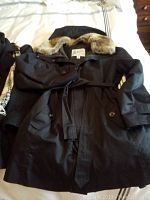 Front view of black London Fog women's XL winter jacket with belt, detachable hood, and faux fur collar laid on bed.