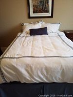 Full view of the queen bed with white duvet cover, gray stripe detail, two white pillows with shams, and navy lumbar cushion at the center.