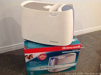 Front and side view of the white Honeywell cool moisture humidifier placed on its original branded box.