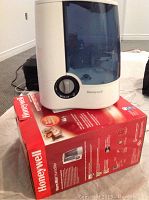 Front and side views of the Honeywell warm mist humidifier placed on its red Honeywell box showing the product and brand details.