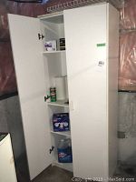 Photo of tall white storage cupboard with door open revealing cleaning supplies and light bulbs on shelves.