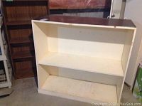 Off-white bookcase angled view showing two large shelves and scuff marks on paint.