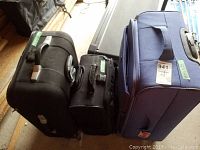 Three suitcases standing vertically close together: blue Tracker spinner, black Samsonite rolling case, black Atlantic carry-on.