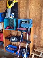 Photo showing a yellow and black life jacket atop blue crates, cleaning tools with blue and red mop heads leaning against a wood shelf