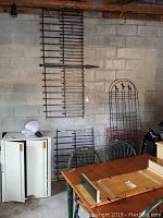 Black metal trellises and garden fencing panels arranged against a concrete block wall with surrounding furniture.