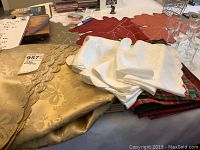 Gold and white damask tablecloths with white napkins stacked on top, displayed on a table with other holiday decor.