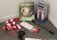 Lot items displayed on carpet including dog collar, leash, black safety belt, decorative sign, Squirrel Buster bird feeder box, and Get Lost Wasp wasp deterrent.