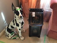 Ceramic Great Dane dog statue sitting next to black metal tin cabinet with floral designs.