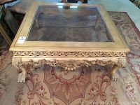 Front and top view showing square coffee table with glass insert on the top surrounded by ornately carved wooden frame and legs